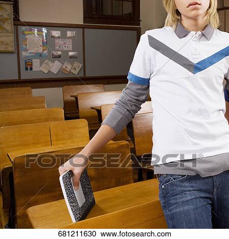 Stock Image - Teenage boy leaning against a chair in a classroom. Fotosearch
