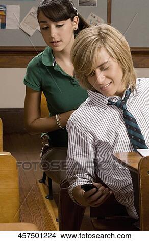 Teenage boy sitting in a classroom and looking at a mobile phone View Large Photo Image Picture - Teenage boy sitting in a classroom and looking at a mobile phone. Fotosearch