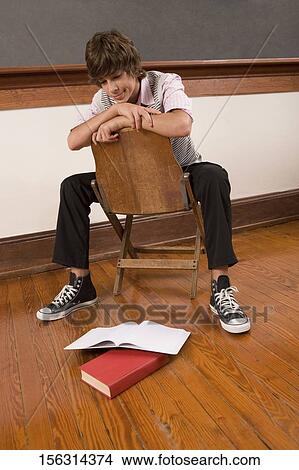 Teenage boy sitting on a chair in a classroom View Large Photo Image Picture - Teenage boy sitting on a chair in a classroom. Fotosearch