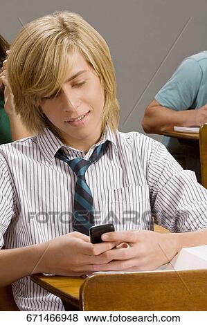 Teenage boy text messaging on a mobile phone in a classroom View Large Photo Image Stock Photo - Teenage boy text messaging on a mobile phone in a classroom. Fotosearch