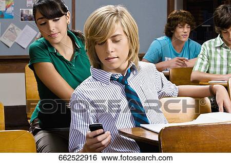 Teenage boy using a mobile phone in a classroom View Large Photo Image Stock Photograph - Teenage boy using a mobile phone in a classroom. Fotosearch