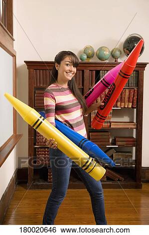 Stock Photograph - Teenage girl holding oversized crayons and smiling. Fotosearch