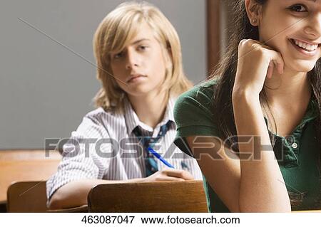 Teenage girl smiling with her classmate sitting behind him View Large Photo Image Stock Photo - Teenage girl smiling with her classmate sitting behind him. Fotosearch