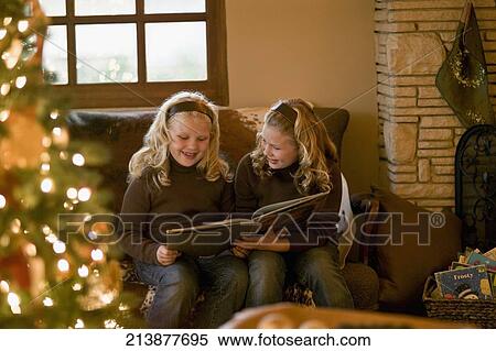Twin sisters looking at photo album in a living room View Large Photo Image Stock Photography - Twin sisters looking at photo album in a living room. Fotosearch