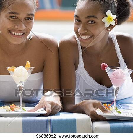 Two female friends holding ice creams at poolside View Large Photo Image Stock Image - Two female friends holding ice creams at poolside. Fotosearch