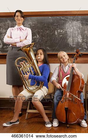 Two girls playing musical instruments with their teacher standing beside them View Large Photo Image Picture - Two girls playing musical instruments with their teacher standing beside them. Fotosearch