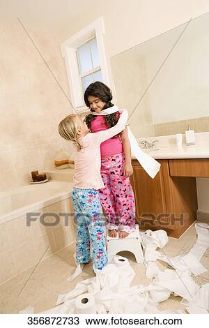 Stock Image - Two girls playing with toilet paper rolls in the bathroom. Fotosearch