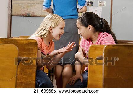 Two schoolgirls gossiping in a classroom View Large Photo Image Stock Photography - Two schoolgirls gossiping in a classroom. Fotosearch