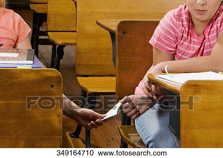 Two schoolgirls passing note during exam in a classroom View Large Photo Image Stock Image - Two schoolgirls passing note during exam in a classroom. Fotosearch