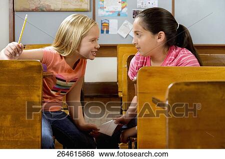 Two schoolgirls passing note during exam in a classroom View Large Photo Image Stock Photo - Two schoolgirls passing note during exam in a classroom. Fotosearch
