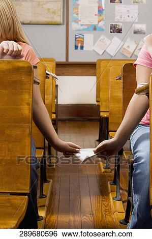 Two schoolgirls passing note during exam in a classroom View Large Photo Image Stock Photograph - Two schoolgirls passing note during exam in a classroom. Fotosearch