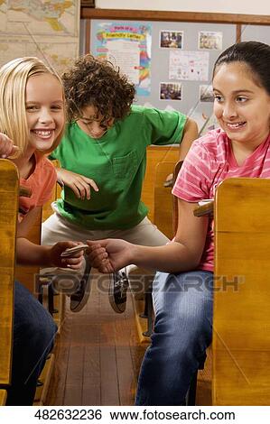 Two schoolgirls passing note during exam in a classroom View Large Photo Image Stock Photograph - Two schoolgirls passing note during exam in a classroom. Fotosearch