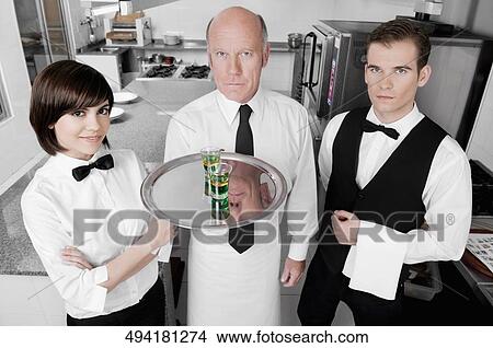 Picture - Two waiters and a waitress standing in the kitchen. Fotosearch
