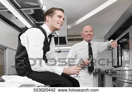 Stock Image - Two waiters drinking wine in the kitchen. Fotosearch