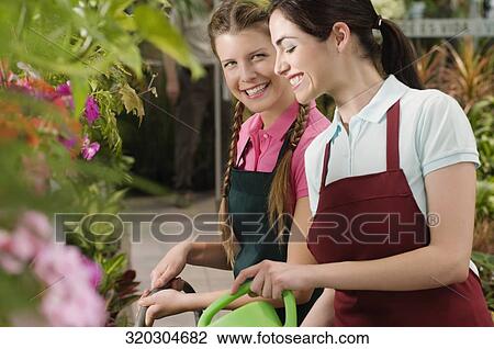 Two women watering plants in a greenhouse View Large Photo Image Stock Image - Two women watering plants in a greenhouse. Fotosearch