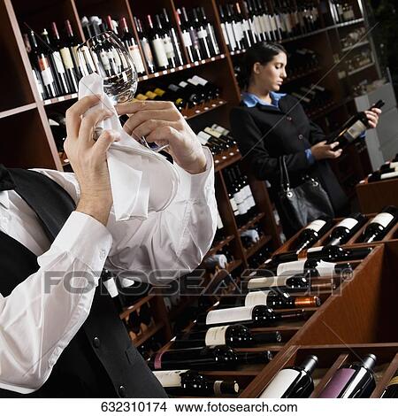 Waiter polishing a wine glass and a businesswoman choosing a bottle in a bar View Large Photo Image Picture - Waiter polishing a wine glass and a businesswoman choosing a bottle in a bar. Fotosearch