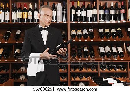 Stock Image - Waiter reading the label of a wine bottle. Fotosearch