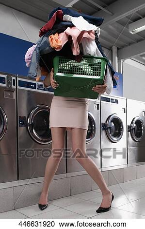 Stock Image - Woman carrying a laundry basket in a laundromat. Fotosearch