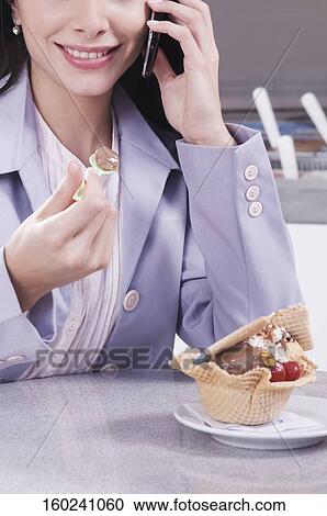 Stock Image - Woman eating ice cream and talking on a mobile phone. Fotosearch