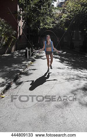 Stock Image - Woman exercising with a jump rope in a street. Fotosearch