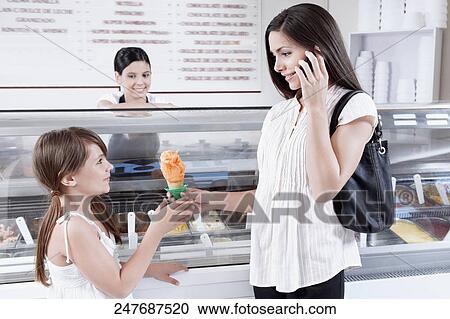 Woman giving ice cream to her daughter and talking on a mobile phone View Large Photo Image Stock Image - Woman giving ice cream to her daughter and talking on a mobile phone. Fotosearch