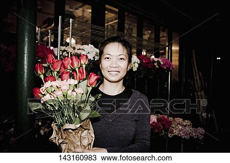 Stock Image - Woman holding a bouquet of flowers at a flowers market, 28 Street, New York City, New York State, USA. Fotosearch