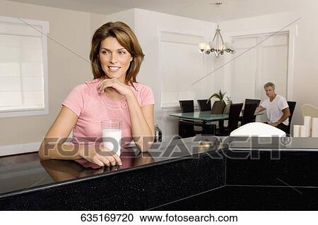 Stock Image - Woman holding a glass of milk and day dreaming. Fotosearch