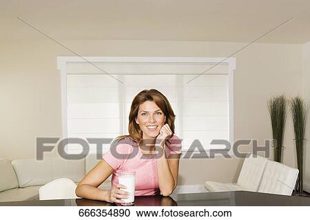 Stock Image - Woman holding a glass of milk and day dreaming. Fotosearch