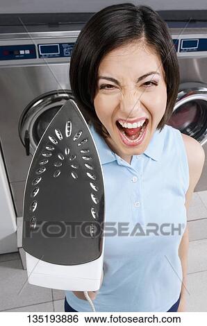 Woman holding an iron in a laundromat View Large Photo Image Stock Photograph - Woman holding an iron in a laundromat. Fotosearch