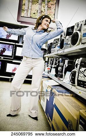 Stock Photography - Woman listening to music system and dancing in a supermarket. Fotosearch