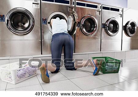 Woman looking inside a washing machine in a laundromat View Large Photo Image Stock Photo - Woman looking inside a washing machine in a laundromat. Fotosearch
