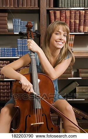 Stock Image - Woman playing a cello in a library. Fotosearch