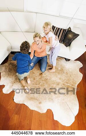 Woman playing with her son and a daughter in a living room View Large Photo Image Stock Photo - Woman playing with her son and a daughter in a living room. Fotosearch