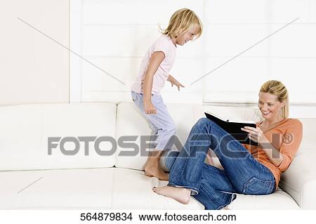 Woman reading a book with her daughter standing beside her View Large Photo Image Picture - Woman reading a book with her daughter standing beside her. Fotosearch