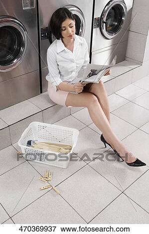 Stock Photo - Woman reading a magazine in a laundromat. Fotosearch