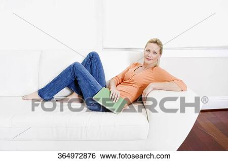 Woman reclining on a couch and holding a book View Large Photo Image Stock Photograph - Woman reclining on a couch and holding a book. Fotosearch