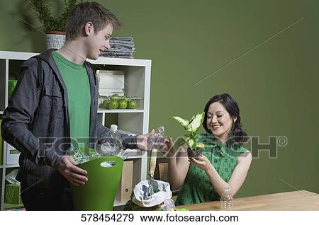 Woman showing a seedling to a man holding a recycling bin beside her View Large Photo Image Stock Photo - Woman showing a seedling to a man holding a recycling bin beside her. Fotosearch