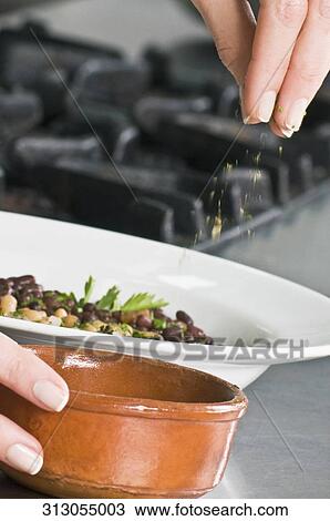 Stock Image - Woman sprinkling cilantro to beans. Fotosearch