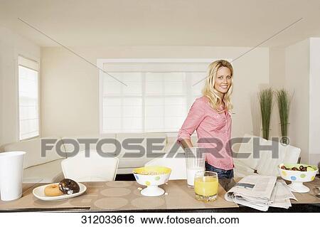 Stock Photograph - Woman standing at a breakfast table and smiling. Fotosearch
