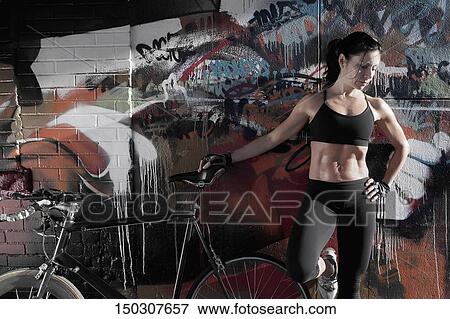 Woman standing with a bicycle in front of a graffiti covered wall View Large Photo Image Stock Photo - Woman standing with a bicycle in front of a graffiti covered wall. Fotosearch