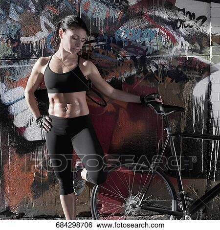 Woman standing with a bicycle in front of a graffiti covered wall View Large Photo Image Stock Photograph - Woman standing with a bicycle in front of a graffiti covered wall. Fotosearch