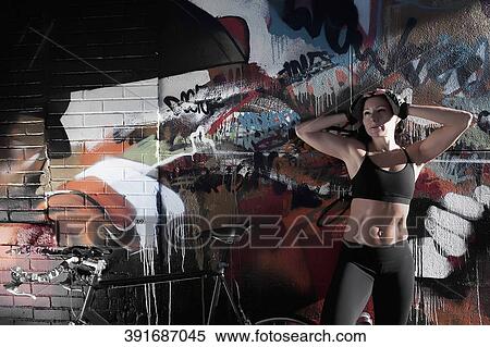 Stock Photography - Woman standing with a bicycle in front of a graffiti covered wall. Fotosearch