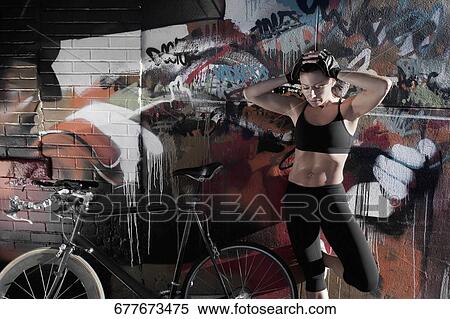 Stock Photography - Woman standing with a bicycle in front of a graffiti covered wall. Fotosearch