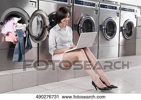 Woman using a laptop in a laundromat View Large Photo Image Stock Image - Woman using a laptop in a laundromat. Fotosearch