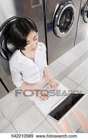Stock Photo - Woman using a laptop in a laundromat. Fotosearch