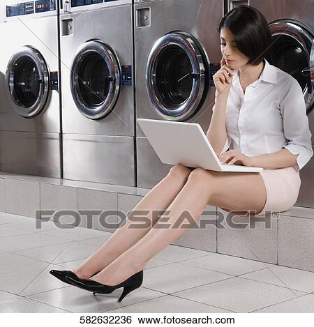 Woman using a laptop in a laundromat View Large Photo Image Stock Photograph - Woman using a laptop in a laundromat. Fotosearch
