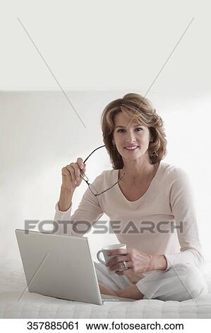 Stock Image - Woman working on a laptop and holding a cup of coffee. Fotosearch