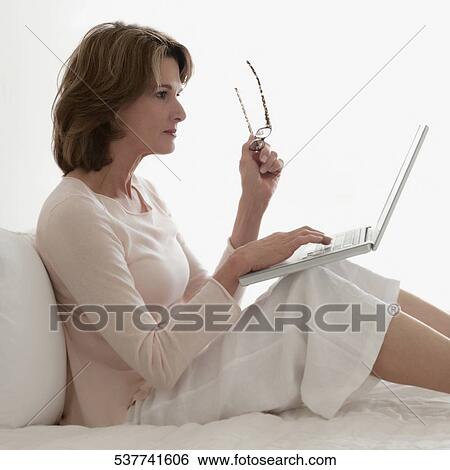Woman working on a laptop on the bed View Large Photo Image Stock Photograph - Woman working on a laptop on the bed. Fotosearch
