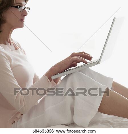 Woman working on a laptop on the bed View Large Photo Image Stock Photograph - Woman working on a laptop on the bed. Fotosearch