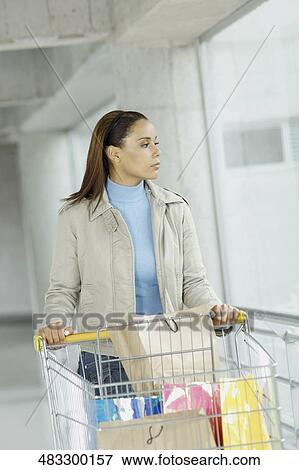 Stock Photo - Young woman standing with a shopping cart. Fotosearch